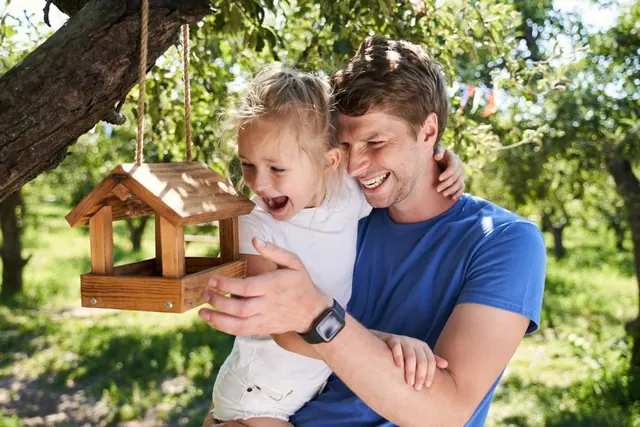 A father and daughter laughing beside a wooden bird feeder