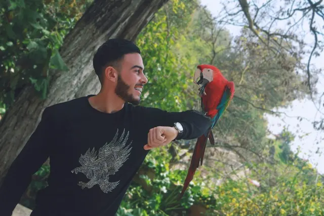 A smiling man with a red macaw perched on his arm